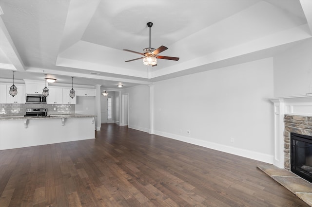 5174 Copse Dr, Augusta, GA 30909 - unfurnished living room with a tray ceiling, a stone fireplace, a ceiling fan, and dark wood-style floors