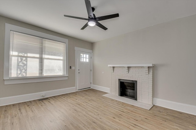 unfurnished living room featuring baseboards, a brick fireplace, visible vents, ceiling fan, and wood finished floors