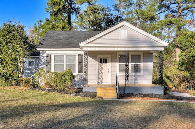 view of front of property with roof with shingles, covered porch, and a front lawn