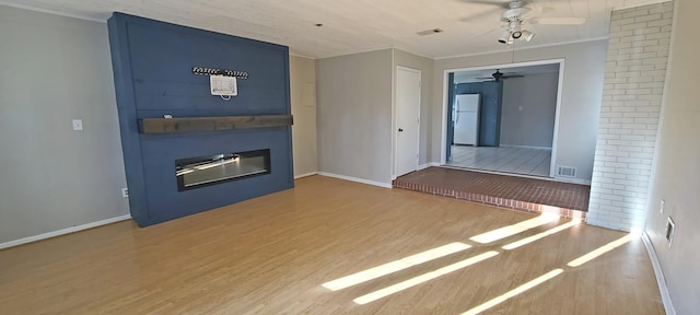 unfurnished living room featuring hardwood / wood-style flooring, crown molding, a large fireplace, and ceiling fan