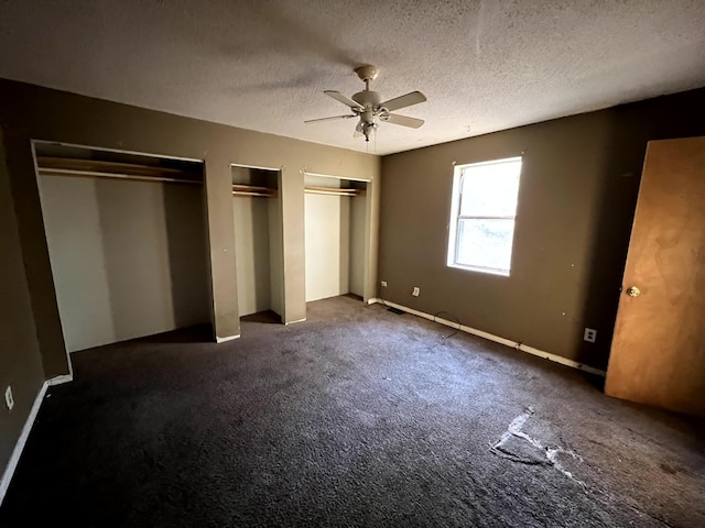 unfurnished bedroom featuring a textured ceiling, ceiling fan, dark carpet, and two closets