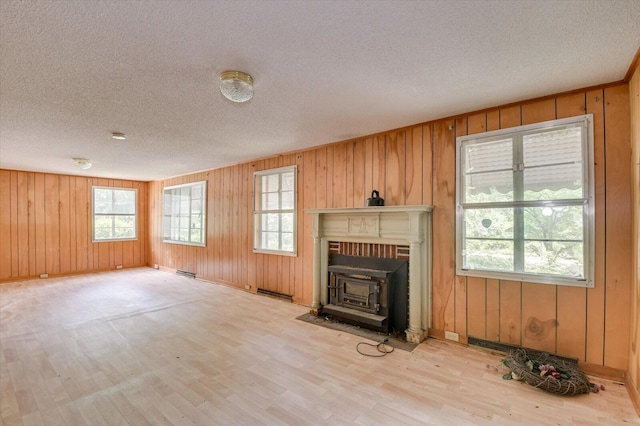 2514 Lumpkin Rd, Augusta, GA 30906 - unfurnished living room with light wood-style flooring, a textured ceiling, wood walls, a wood stove, and visible vents