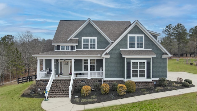 view of front facade featuring roof with shingles, a porch, and a front yard