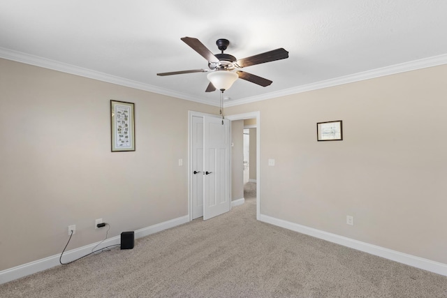 carpeted spare room with ornamental molding, a ceiling fan, and baseboards