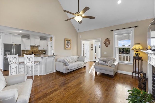 living room featuring baseboards, ceiling fan, dark wood-type flooring, a fireplace, and high vaulted ceiling