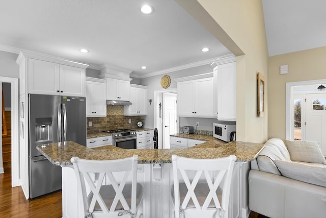 kitchen featuring under cabinet range hood, a peninsula, white cabinetry, appliances with stainless steel finishes, and tasteful backsplash