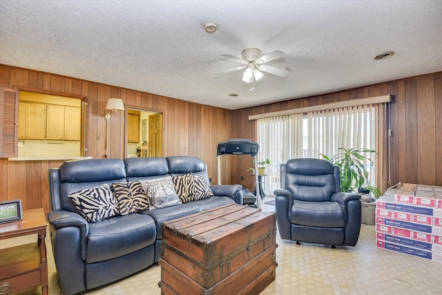 living room with ceiling fan, a textured ceiling, and wooden walls