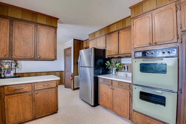 kitchen featuring stainless steel fridge, a textured ceiling, double oven, and wooden walls