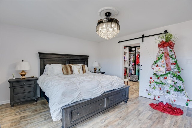 bedroom featuring light wood-type flooring, a barn door, and a chandelier