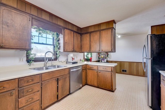 kitchen featuring sink, kitchen peninsula, wood walls, a textured ceiling, and appliances with stainless steel finishes