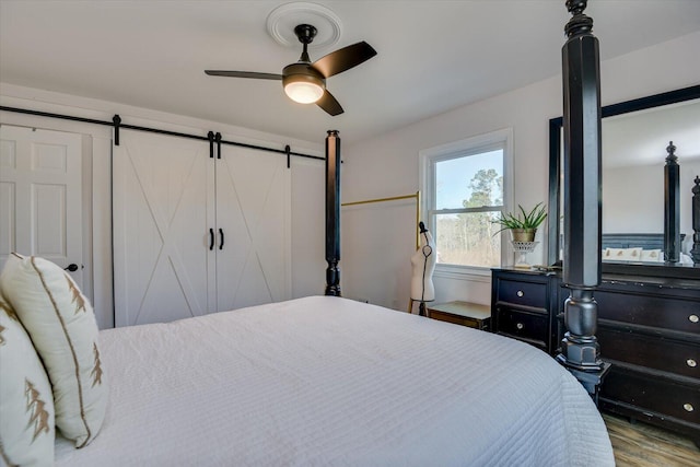 bedroom with hardwood / wood-style flooring, ceiling fan, and a barn door