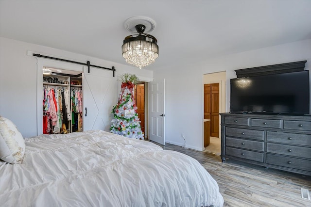 bedroom featuring a barn door, a closet, light hardwood / wood-style floors, and an inviting chandelier