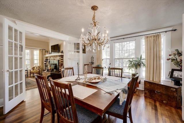 dining space featuring a glass covered fireplace, dark wood-style flooring, an inviting chandelier, a textured ceiling, and french doors