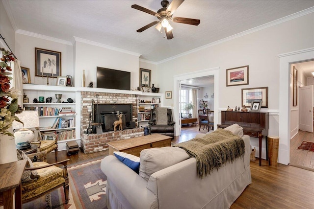 living area with crown molding, a fireplace, ceiling fan, and wood finished floors