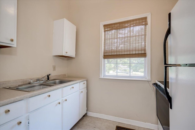 kitchen featuring light countertops, freestanding refrigerator, white cabinets, a sink, and baseboards