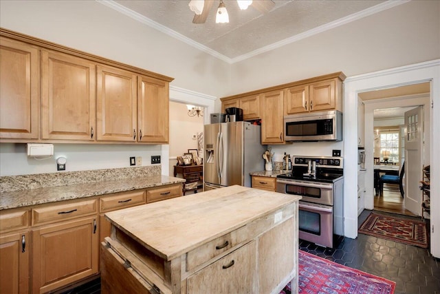 kitchen featuring ceiling fan, light stone counters, a kitchen island, ornamental molding, and appliances with stainless steel finishes