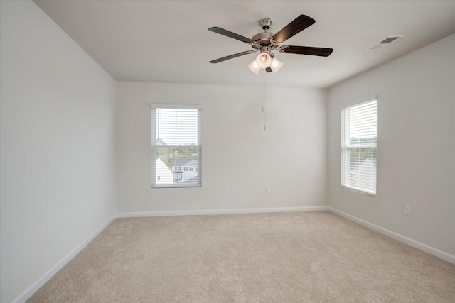 empty room featuring ceiling fan, light colored carpet, and a wealth of natural light