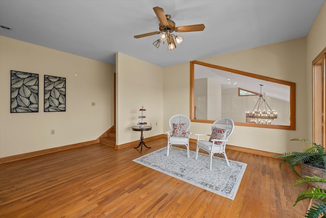 sitting room with hardwood / wood-style floors and ceiling fan with notable chandelier