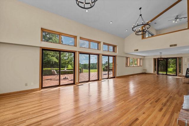 unfurnished living room with a high ceiling, ceiling fan with notable chandelier, and light wood-type flooring