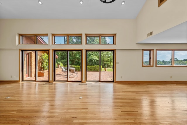 unfurnished living room with a wealth of natural light, light hardwood / wood-style flooring, and a high ceiling