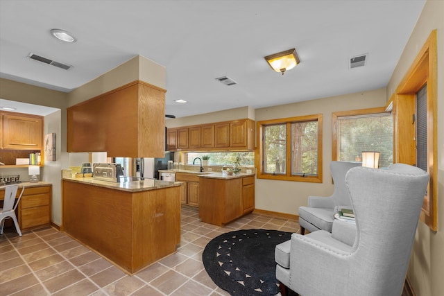 kitchen with kitchen peninsula, light tile patterned floors, light stone counters, and sink