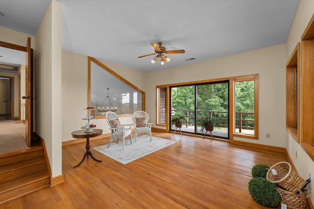 living area featuring ceiling fan with notable chandelier and light hardwood / wood-style floors