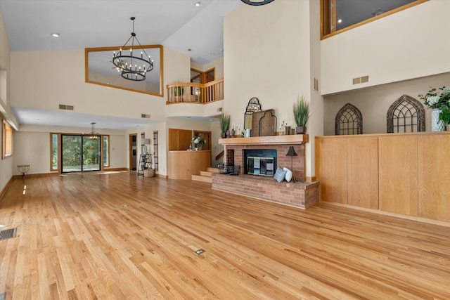 living room with a fireplace, a high ceiling, light wood-type flooring, and a chandelier