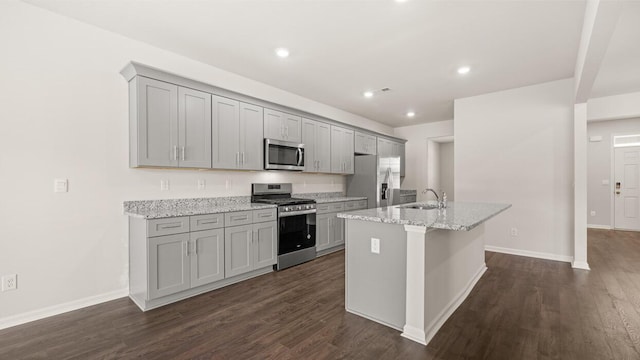 kitchen featuring sink, stainless steel appliances, gray cabinets, light stone countertops, and a kitchen island with sink