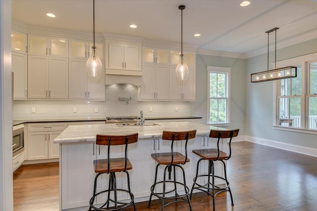 kitchen with crown molding, sink, a center island with sink, white cabinets, and stainless steel microwave