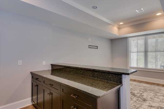 kitchen featuring kitchen peninsula, dark stone countertops, ornamental molding, and light wood-type flooring