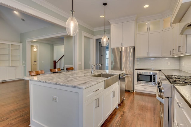 kitchen with backsplash, a center island with sink, white cabinetry, and high end appliances