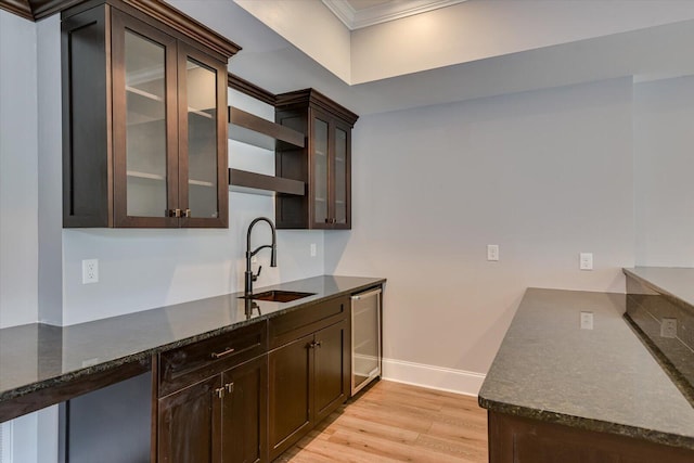 kitchen featuring dark stone counters, crown molding, sink, light hardwood / wood-style flooring, and dark brown cabinets