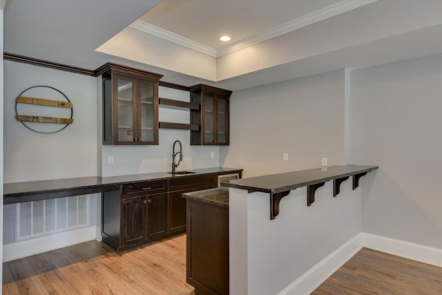 kitchen with sink, light wood-type flooring, ornamental molding, a kitchen bar, and kitchen peninsula