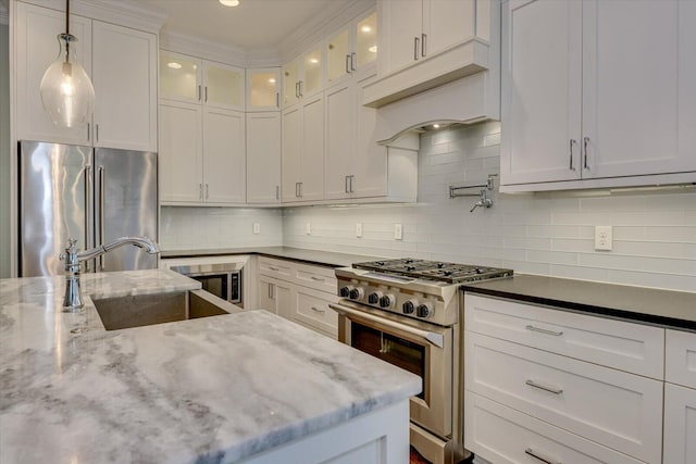 kitchen featuring sink, premium appliances, tasteful backsplash, dark stone countertops, and white cabinets