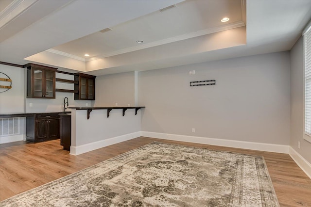 kitchen featuring a breakfast bar, dark brown cabinets, light hardwood / wood-style floors, and a raised ceiling