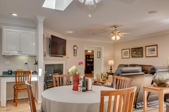 dining room featuring a skylight, ceiling fan, a tile fireplace, and ornamental molding