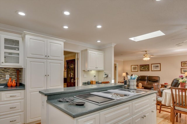 kitchen featuring a skylight, white cabinetry, ceiling fan, cooktop, and crown molding