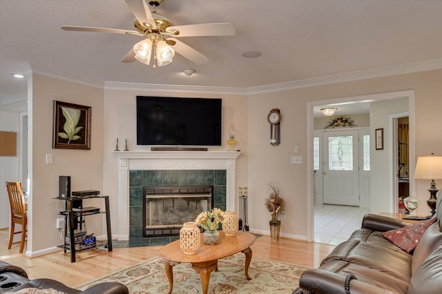 living room with a tiled fireplace, ceiling fan, light hardwood / wood-style floors, and ornamental molding