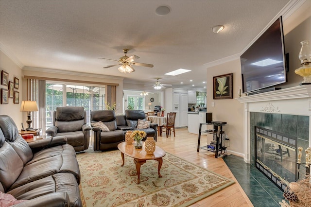 living room with ceiling fan, a high end fireplace, wood-type flooring, a textured ceiling, and ornamental molding