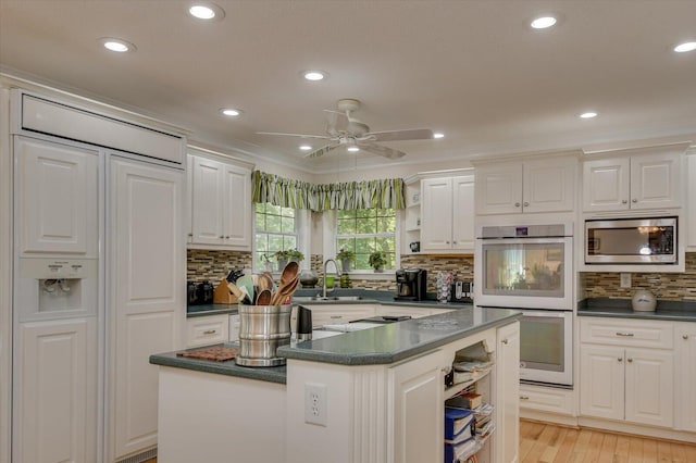 kitchen with ceiling fan, stainless steel microwave, white double oven, a kitchen island, and white cabinets