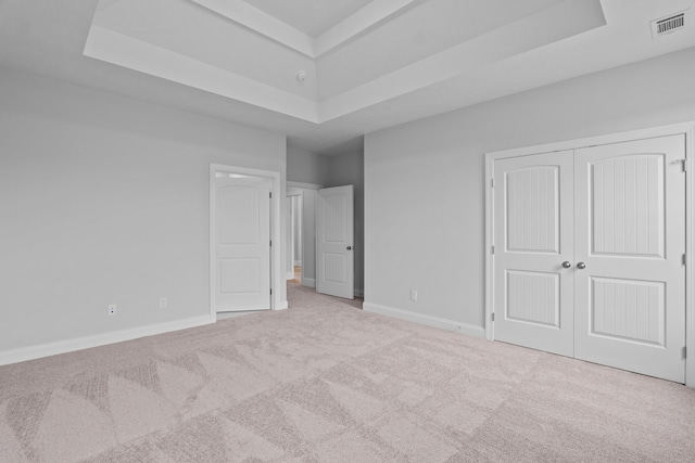 unfurnished bedroom with a tray ceiling, a closet, and light colored carpet