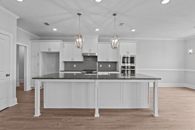 kitchen with a large island, a breakfast bar, white cabinets, and dark stone counters