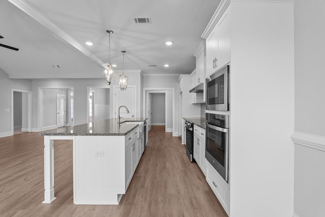 kitchen with white cabinetry, hanging light fixtures, stainless steel appliances, a kitchen bar, and a center island with sink