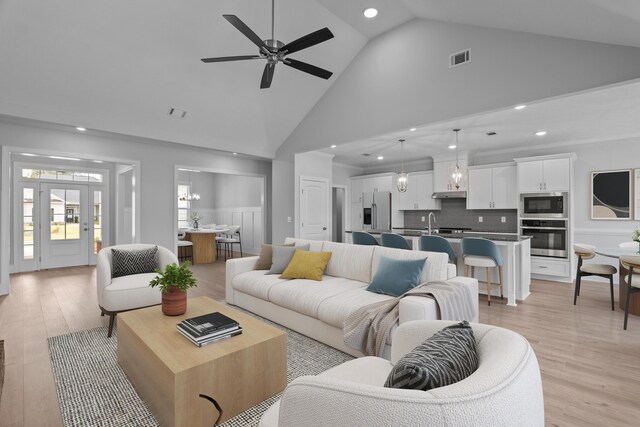 unfurnished living room with light hardwood / wood-style flooring, high vaulted ceiling, ceiling fan with notable chandelier, and sink