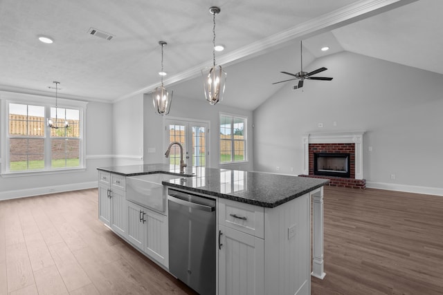 kitchen featuring pendant lighting, dishwasher, a kitchen island with sink, white cabinets, and a brick fireplace