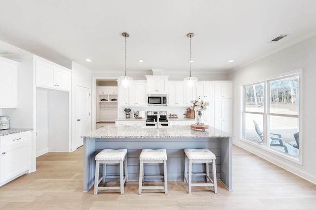 kitchen featuring white cabinetry, appliances with stainless steel finishes, decorative light fixtures, and a kitchen island with sink