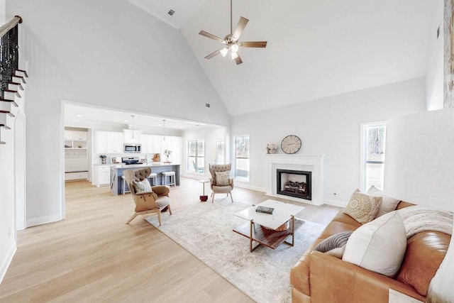 living room with ceiling fan, high vaulted ceiling, and light hardwood / wood-style flooring