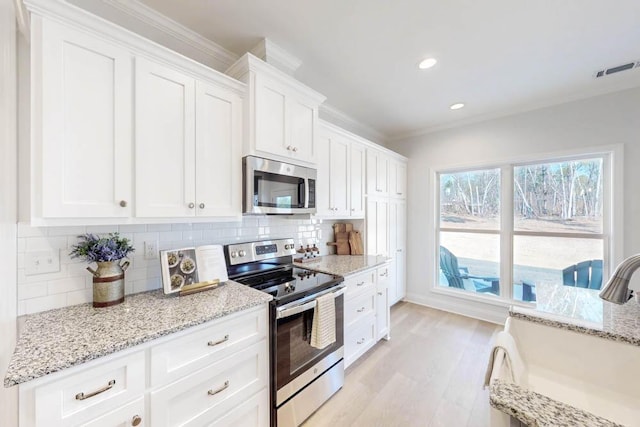 kitchen with sink, appliances with stainless steel finishes, white cabinetry, backsplash, and light hardwood / wood-style floors