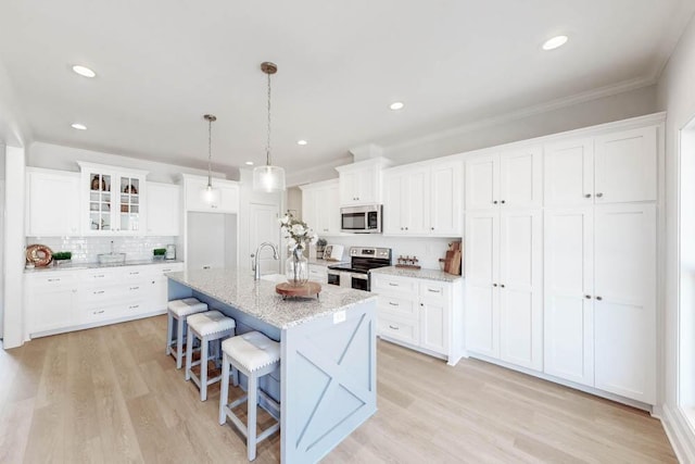 kitchen with appliances with stainless steel finishes, a kitchen island with sink, hanging light fixtures, light stone countertops, and white cabinets