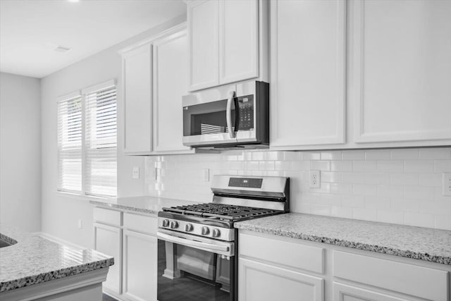 kitchen with tasteful backsplash, appliances with stainless steel finishes, light stone counters, and white cabinetry